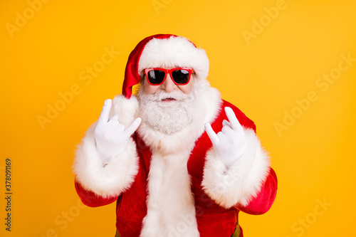 Close-up portrait of his he nice funny cool naughty white-haired Santa St Nicholas showing double horn sign heavy metal isolated over bright vivid shine vibrant yellow color background