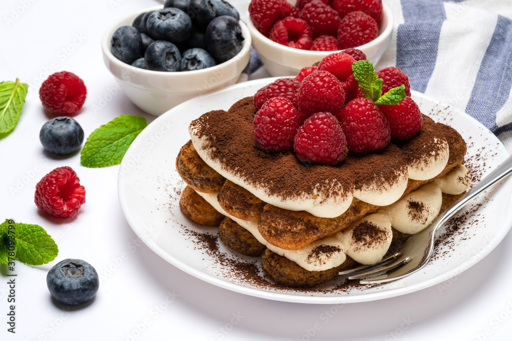 portion of Classic tiramisu dessert with raspberries and blueberries on ceramic plate isolated on white portion of Classic tiramisu dessert with raspberries and blueberries on ceramic plate isolated on white