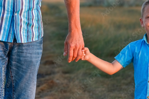 A Hands of a happy child and parent in nature in a park by the road