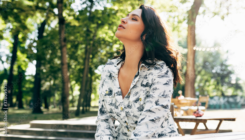 Outdoor horizontal image of a beautiful young woman takes a break, has a dreamy expression while looking up to the sky. Pretty girl resting in the park on a sunny day. Outdoor horizontal image of a beautiful young woman takes a break, has a dreamy expression while looking up to the sky. Pretty girl resting in the park on a sunny day.