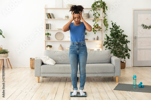 Unhappy Girl Standing On Scales Having Excess Weight Posing Indoors