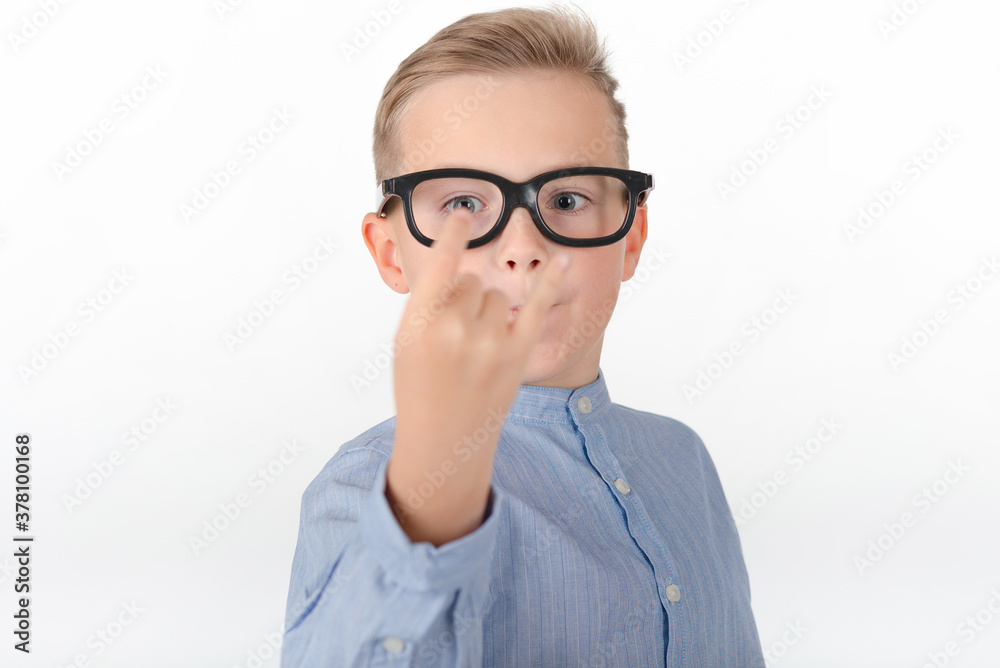 Young Caucasian boy in glasses,blue shirt and shows hands with rock gesture.Studio portrait,white wall.