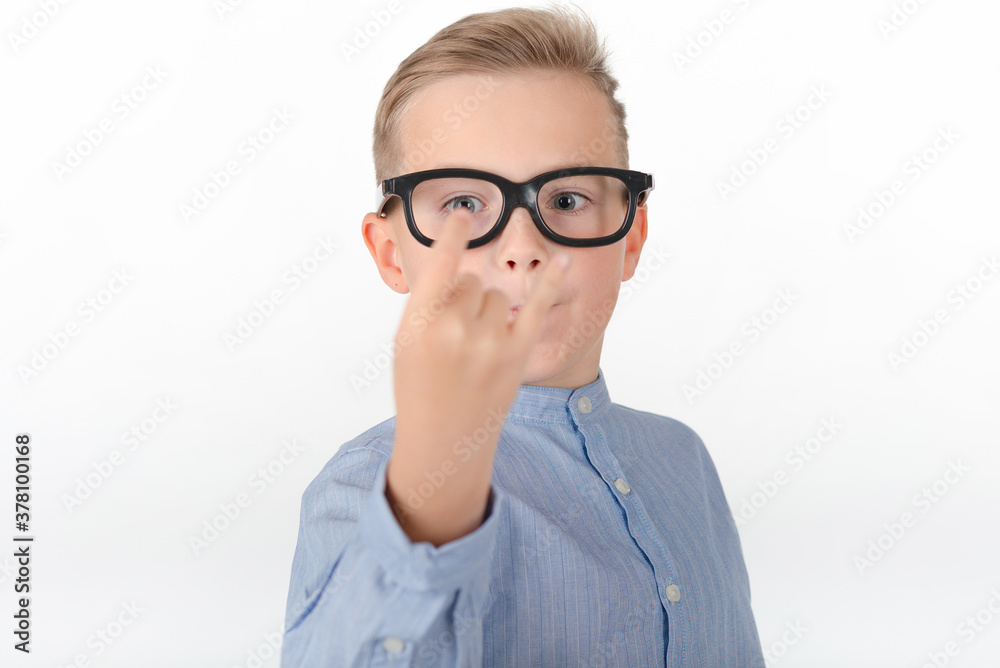 Young Caucasian boy in glasses,blue shirt and shows hands with rock gesture.Studio portrait,white wall. Young Caucasian boy in glasses,blue shirt and shows hands with rock gesture.Studio portrait,white wall.