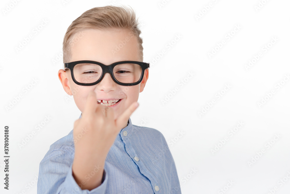 Young Caucasian boy in glasses,blue shirt and shows hands with rock gesture.Studio portrait,white wall. Young Caucasian boy in glasses,blue shirt and shows hands with rock gesture.Studio portrait,white wall.