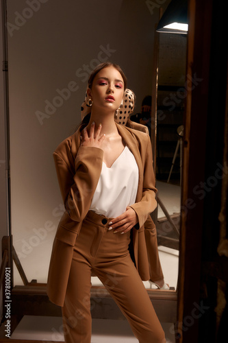 Tall slim elegant fashion teenager model wearing brown male style over size suit and polka dot kerchirfwith trendy makeup and brunette hair in tail. Fashionable portrait with mirrors and reflections