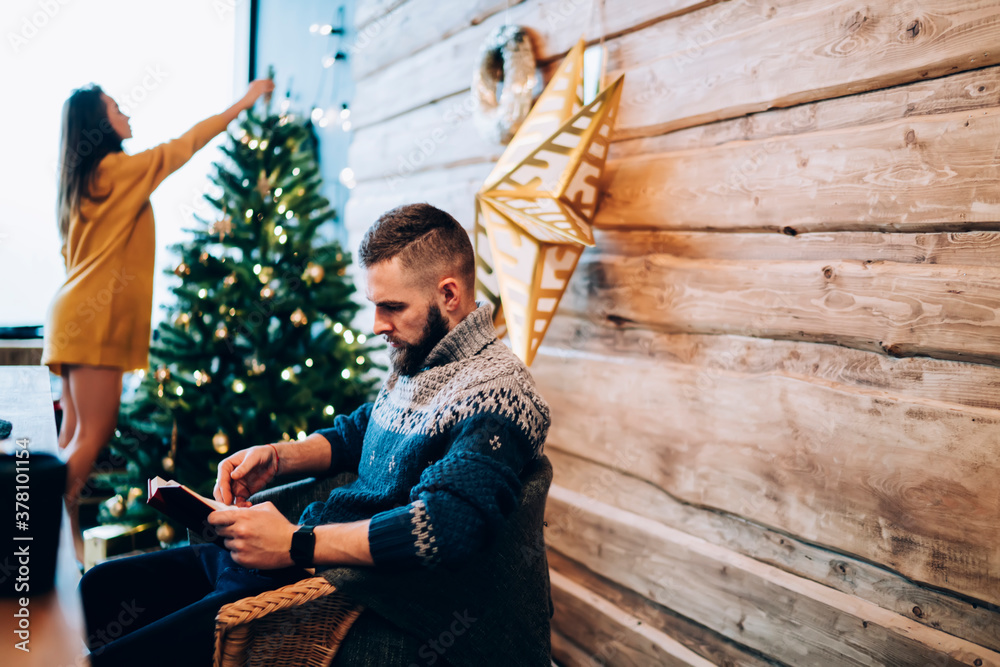 Serious couple decorating fir tree and reading book Serious couple decorating fir tree and reading book