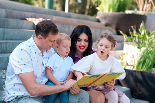 Happy young family with two kids sitting in the park reading a book