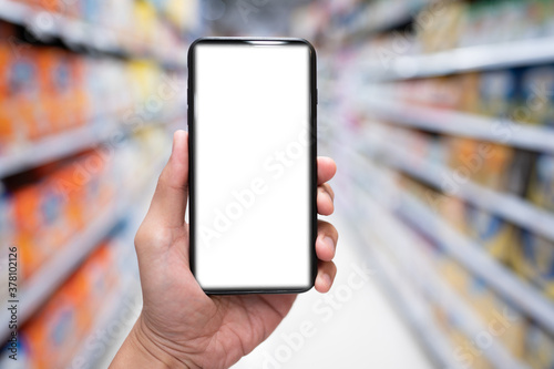 Hand holding mobile smartphone empty touch screen on supermarket or convenience stores background.Blank free word,Copy space for text.Use for your advertisement design or mock up text.Business concept