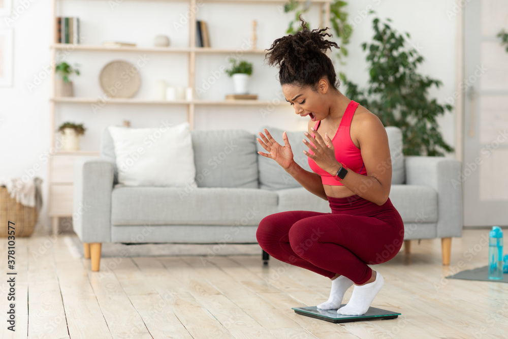 Unhappy Black Woman Shouting Standing On Weight-Scales Indoors Unhappy Black Woman Shouting Standing On Weight-Scales Indoors
