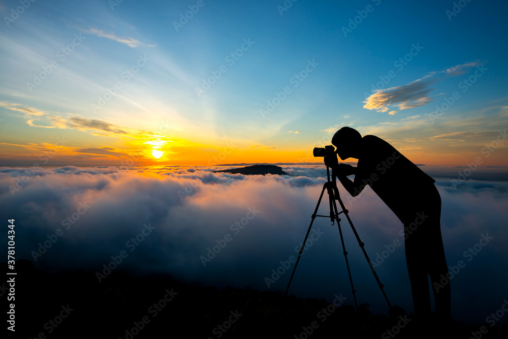 A photographer standing on top of Mountain at sunset with vivid clouds with mist.