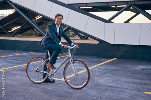 Happy young man in formal suit riding bicycle on street