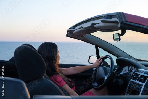 Young woman driving convertible car during sunset and enjoy, back view, holding the steering wheel with one hand