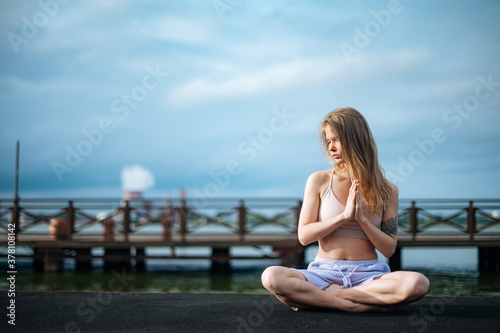 Yoga practice and meditation in nature in sunrise. Woman practicing near City on pier.