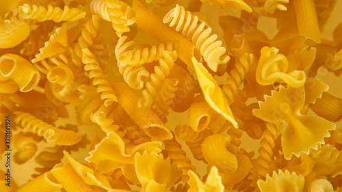 Freeze motion of flying uncooked italian pasta fusilli on golden background.