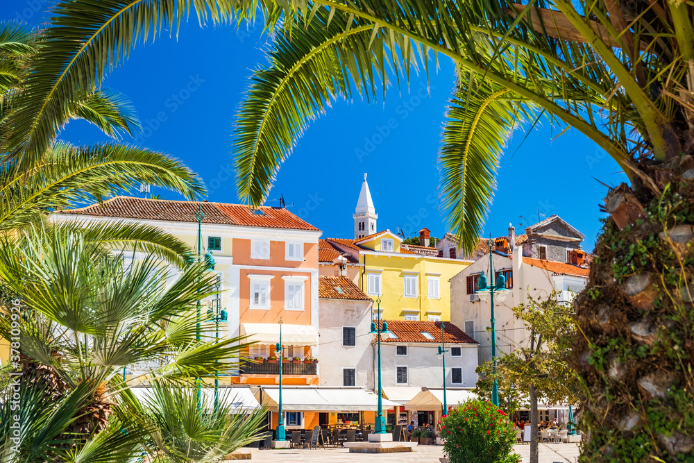 Town of Mali Losinj on the island of Losinj, Adriatic coast in Croatia, cathedral tower and city center, view through the palm leaves
