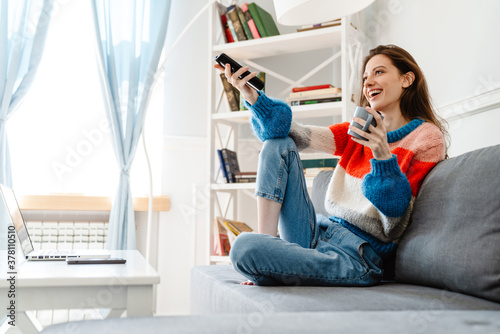 Photo of girl drinking coffee and using remote control while watching tv