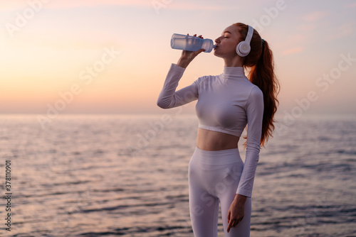 Image of sportswoman in headphones drinking water while working out