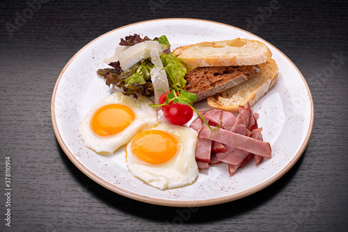 Fried fried eggs with tomatoes  ham and ciabatta toast  on a dark background. Breakfast