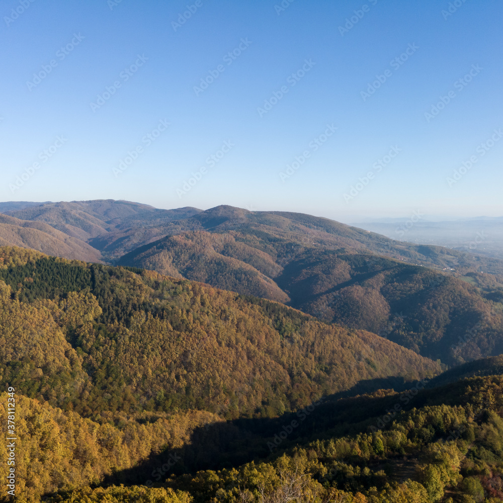 Scenic view from the slope of the Kozara mountain overgrown with forest during a sunny day against the blue sky.