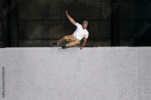 Fotografie Young strong parkour and freerunning athlete jumping over the wall in urban environment