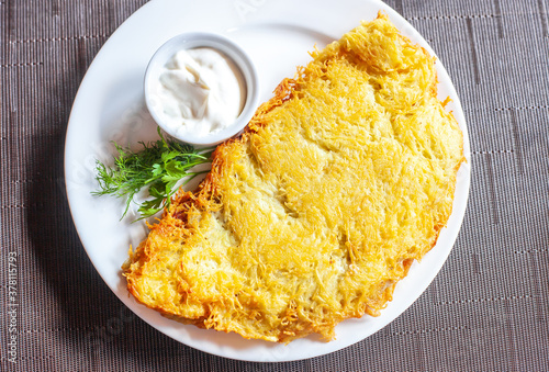 Big potato pancake with sour cream and green parsleys, top view