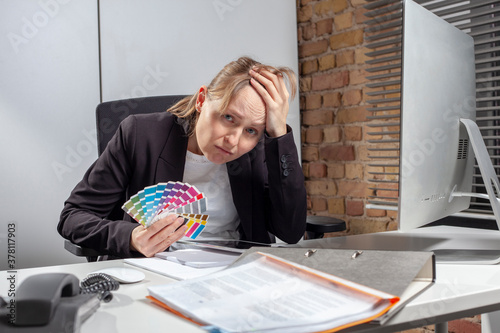 Young woman at work with a colorful palette in her hand is completely exhausted to find a decision for a suitable color selection for the next important big project photo