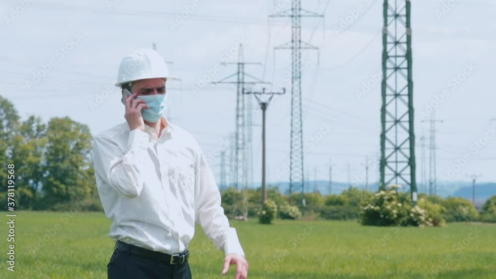 Masked power lines engineer perform regular services, talk by phone keeping physical distance. Protect members and employees during the pandemic. Power lines inspections during quarantine time. Masked power lines engineer perform regular services, talk by phone keeping physical distance. Protect members and employees during the pandemic. Power lines inspections during quarantine time.