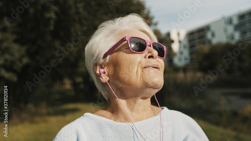 Senior woman with pink sunglasses in the park looking at the distance. High quality photo