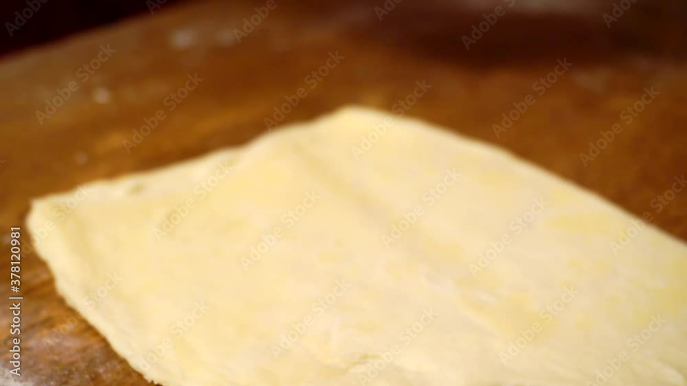hands roll out a sheet of dough with a rolling pin on a wooden table.