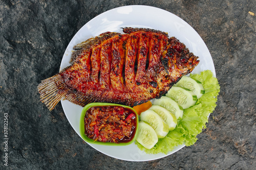 Delicious grilled tilapia (nila bakar) from indonesia with rice, tempeh, vegetables, and chilli sauce in plate photo