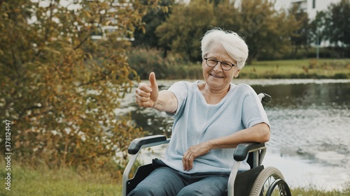 Senior gray haired lady in the wheelchair neear the river showing thumbs up. High quality photo photo