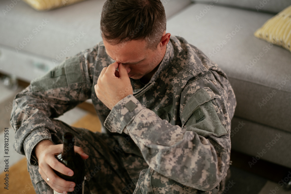 Fototapeta premium Depressed soldier with bottle sitting in livig room., Alcohol addiction...