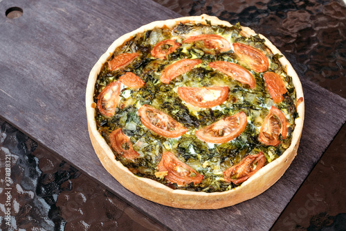 Pie with spinach and tomatoes lies on table. Homemade pie for the whole company made from vegetables.