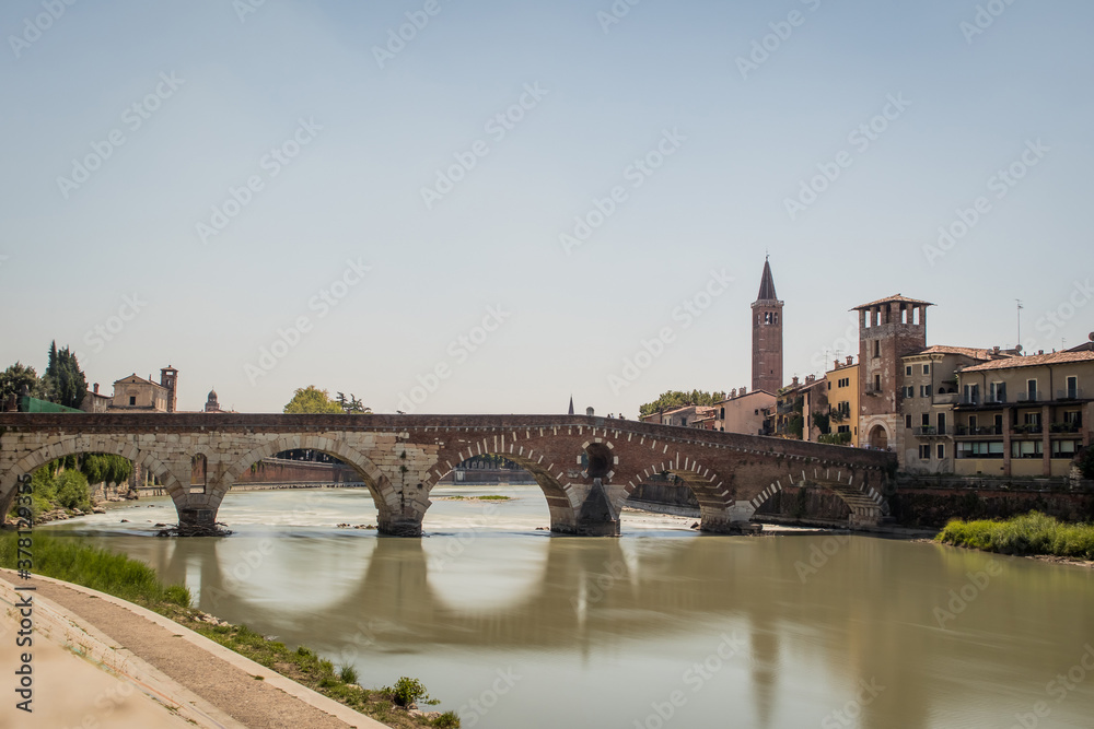 view of the famous Ponte Pietra in Verona, rising above the river of Adige in Italy. Long exposure daylight shot on a sunny day of an old brick bridge.