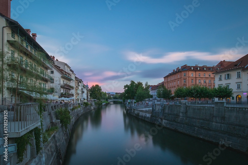 River banks of Ljubljanica with colorful houses during early hours of the evening. Blue hour viewed from the bridge in Ljubljana, looking south towards thethe other bridge.