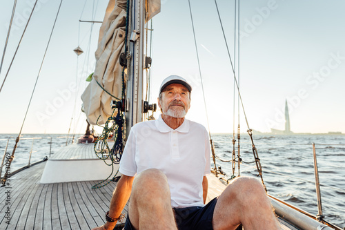Relaxed mature man sitting on his yacht. Yachtsman resting on the boat at sunset and looking away.