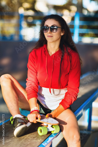 Young woman in sunglasses is resting on the sports ground for skateboarding on a summer sunny evening © Sergey Chayko