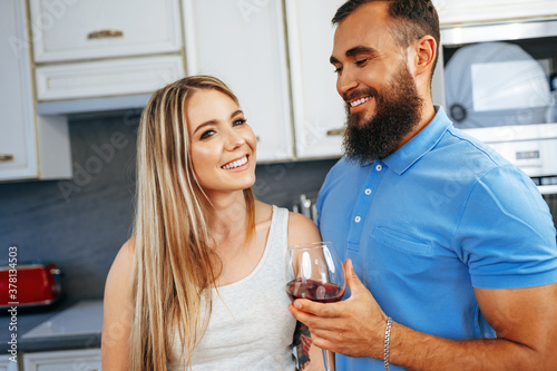 Cheerful smiling couple cooking and drinking wine in kitchen