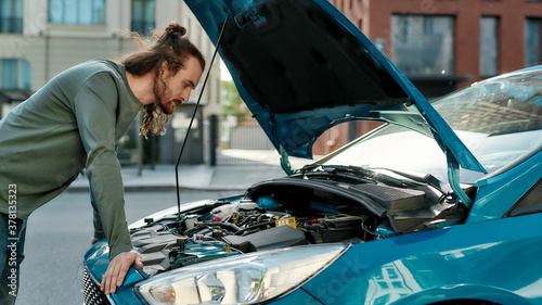 Foto Young man looking focused, examining his broken car with open hood while standin