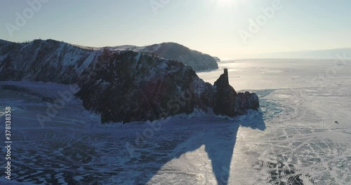 Aerial view of Shamanka rock and Cape Burkhan at sunset on frozen lake Baikal, Olkhon island in winter. Khuzhir, Siberia, Russia. Landscape of Russian natural landmark. 