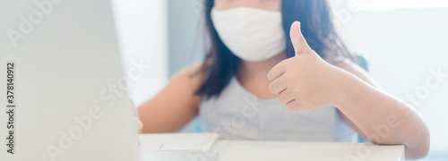 Asian girl student thumb up wearing mask study online learning online education video call zoom.learn english online with laptop at home.New normal.Covid-19 coronavirus.Social distancing.stay home.