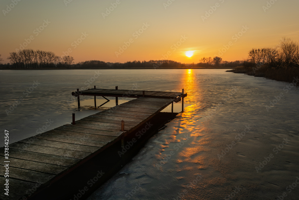 Beautiful evening view of the wooden platform on the frozen lake at sunset.