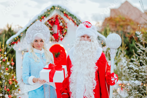 Santa Claus and snow maiden with a gift in their hands pose in the snow photo