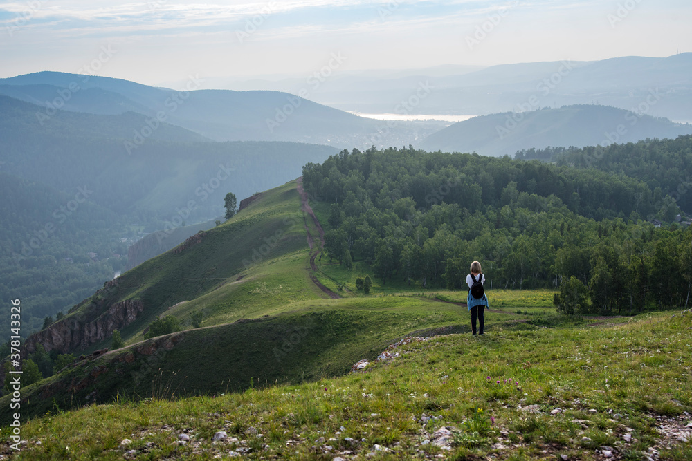 Fototapeta premium Nature photographer tourist with camera shoots while standing on top of the mountain. Beautiful summer nature on sunset.