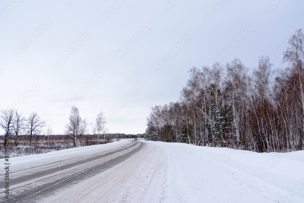 Patterns on the winter highway in the form of four straight lines. Snowy road on the background of snow-covered forest. Winter landscape.