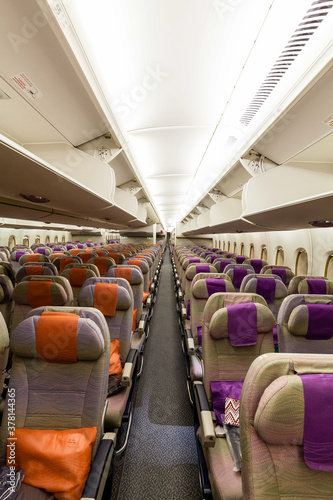 Looking down the aisle of a wide modern wide body jet aircraft, overhead bins open and empty economy seats waiting for passengers.