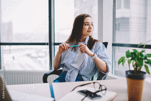 Contemplative female freelance copywriter sitting at table desk with cropped netbook and pondering looking away while thinking about journalistic ideas, thoughtful woman in smart casual wear dreaming