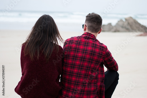 Couple from behind on a beach looking out to sea on a cloudy day