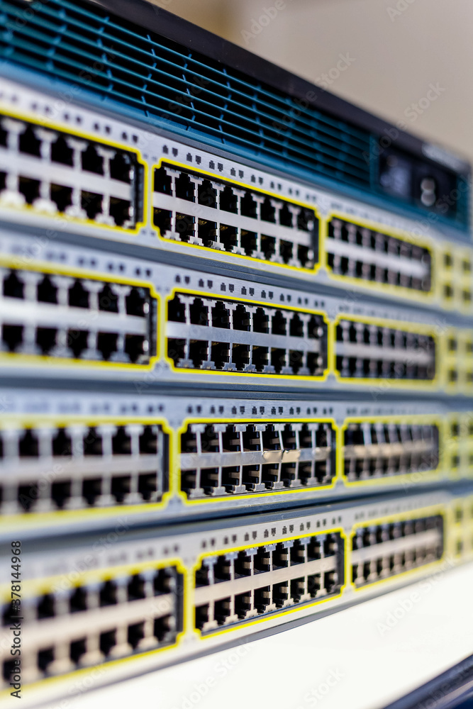 A stack of network switches topped with a router that has empty ports exposed just removed from a server cabinet in an office.