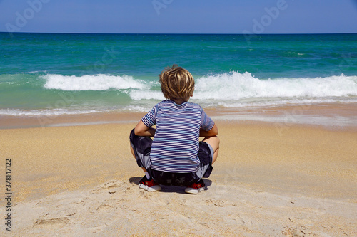 Boy crouching on a Florida beach, looking out at the turquoise ocean